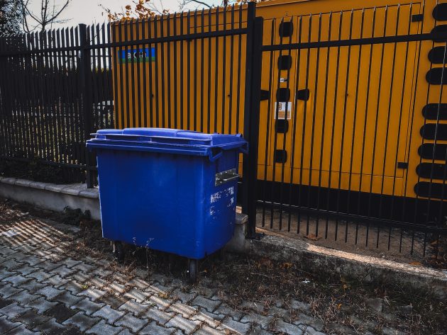 Blue commercial dumpster rental parked beside black metal safety fence