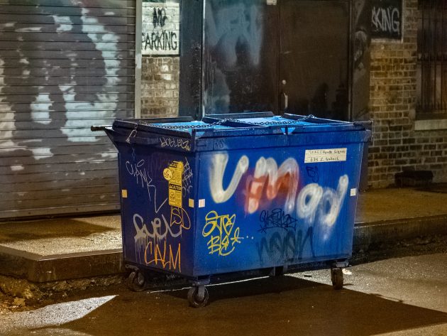 Blue commercial dumpster rental with graffiti tags in alleyway