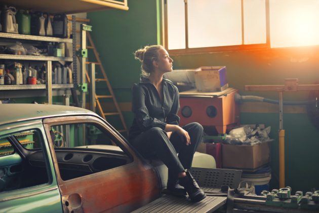 Woman sitting on classic car body during garage declutter project