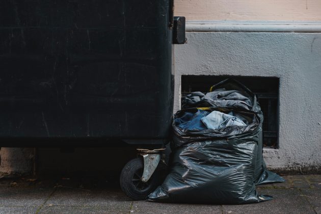 Black small dumpster rental with trash bags on urban sidewalk