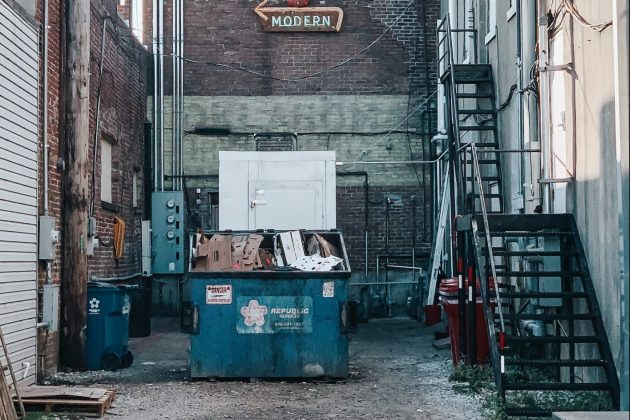 Blue commercial front-load dumpster filled with cardboard in alleyway
