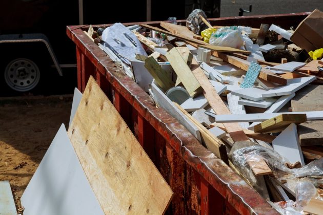 Wood construction debris filling a red roll-off dumpster rental container