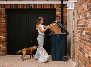 Woman throwing away waste into dumpster during residential cleanup project